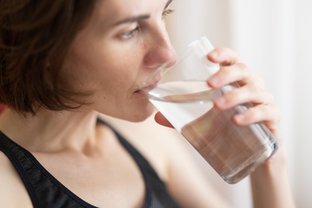 A woman drinking water from a clear glass, promoting the importance of staying hydrated